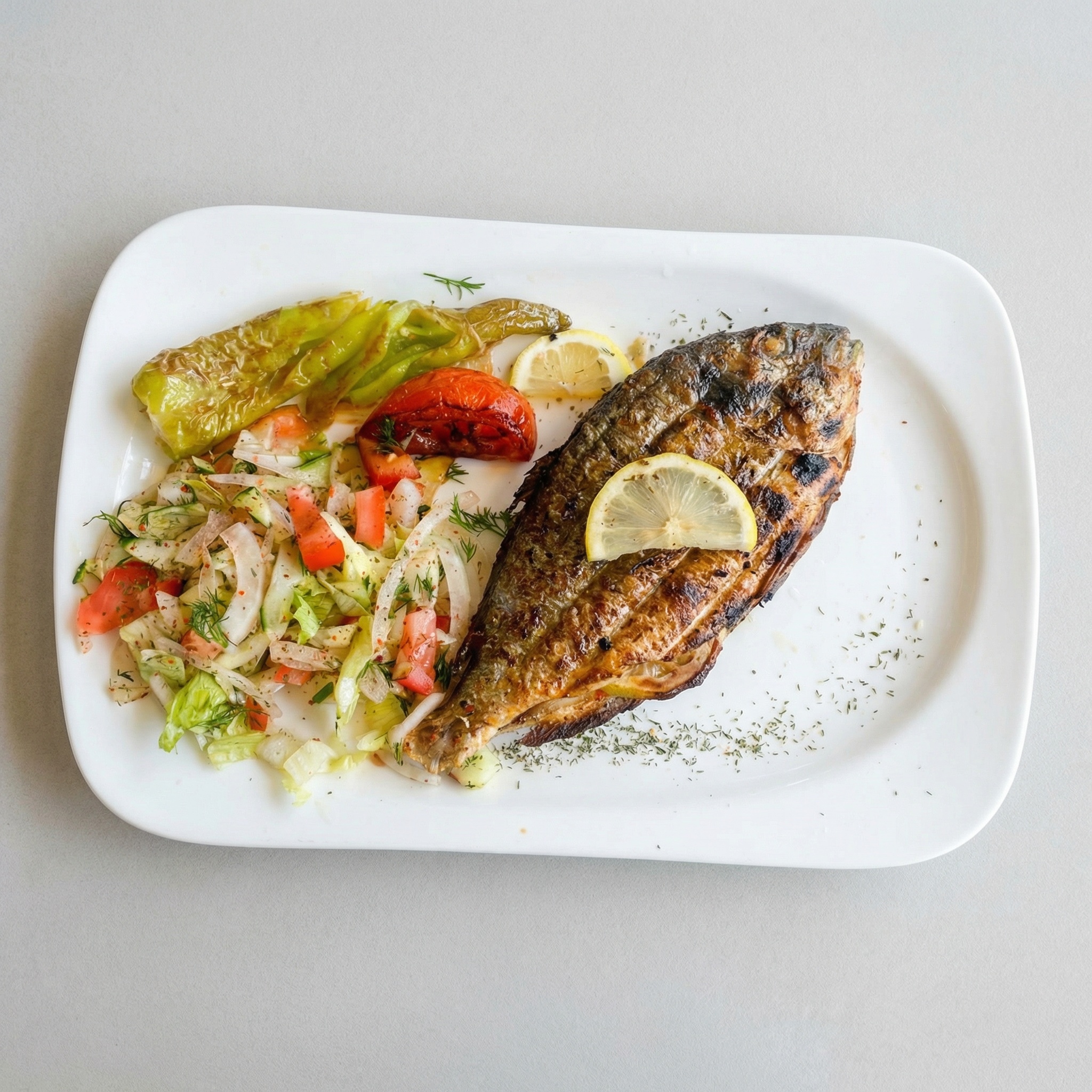 Eine im Ganzen gegrillte Dorade auf einem weißen Teller, angerichtet mit Zitronenscheibe, gemischtem Salat und gegrilltem Gemüse.