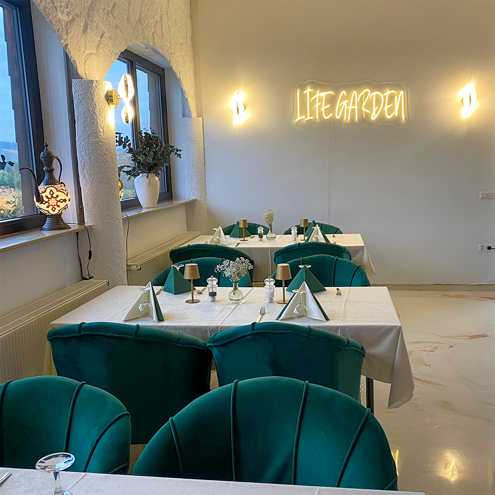 Moderne Restaurant-Bestuhlung in Petrol-Grün mit dem leuchtenden Schriftzug "Life Garden".