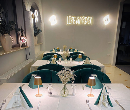 Festlich gedeckter Tisch im Life Garden mit eleganten grünen Samtsesseln und Blumen.